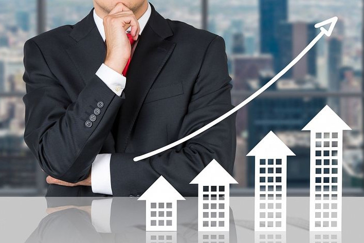 Real Estate Management||Mann im Anzug mit Hand nachdenklich vor dem Kinn plaziert. Vor ihm eine Grafik mit steigendem Pfeil und Häusern