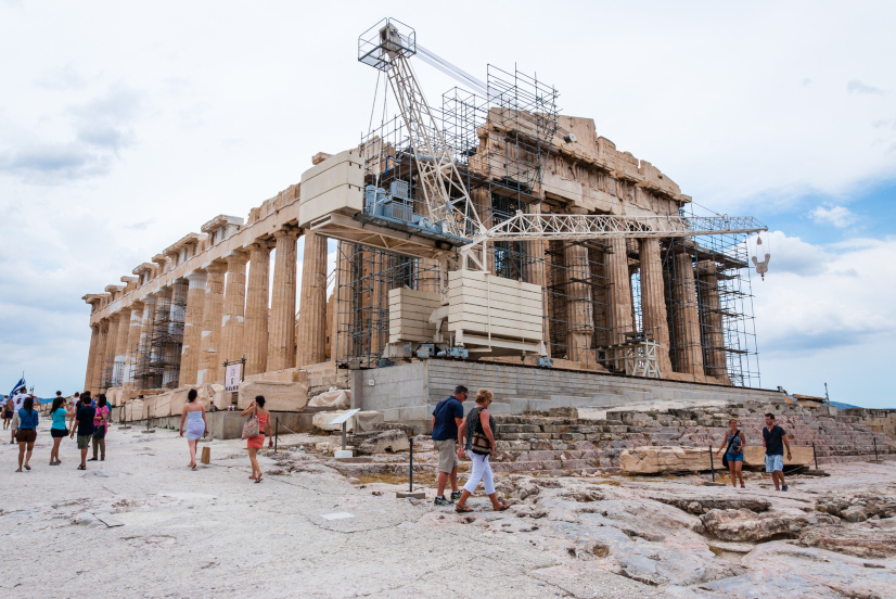 Der berühmte Parthenon auf dem Akropolis-Hügel unter Rekonstruktion umgeben von Baugerüst und stehendem Baukran in der Vorderseite des Tempels mit gehenden Touristen