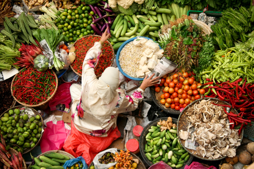 Asiatische Frau sitzt am Bauernmarkt inmitten von Gemüse
