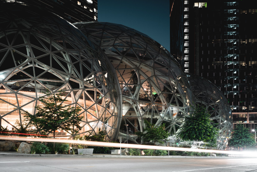 The exterior of The Spheres, Seattle, at night, glass in honeycomb structured panels that reveals plantlife inside.