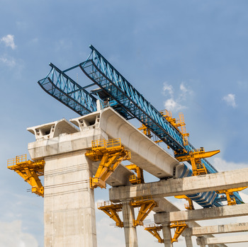 A panoramic view of a bridge construction site with concrete piers and columns rising up from the ground, surrounded by scaffolding and construction equipment.