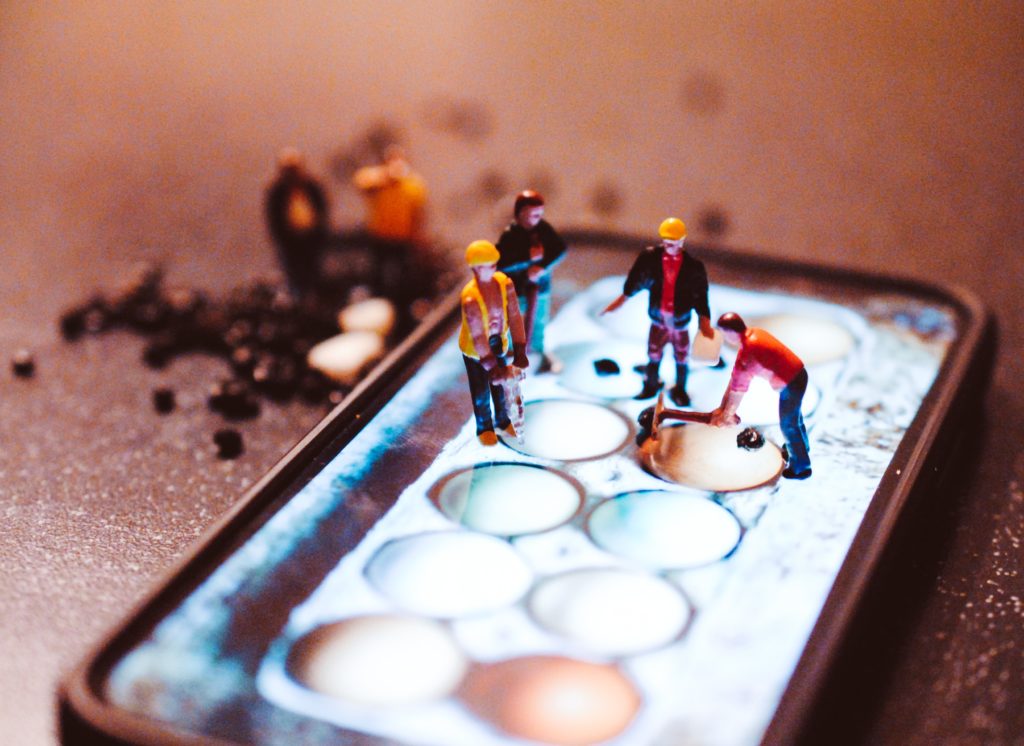 Miniature construction workers stand on a smart phone.
